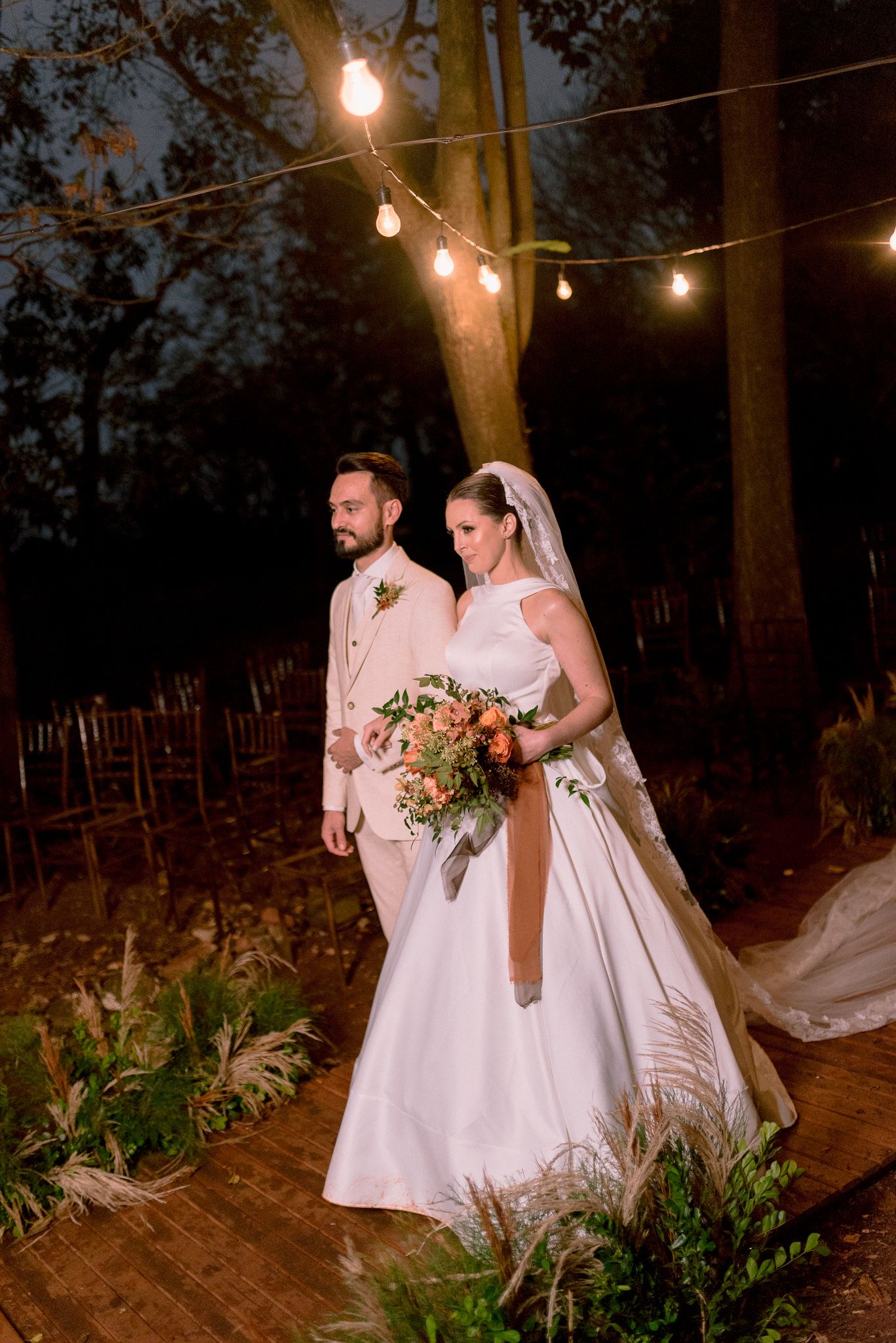 Wedding couple strolling along a romantic path lit by overhead bistro lights.