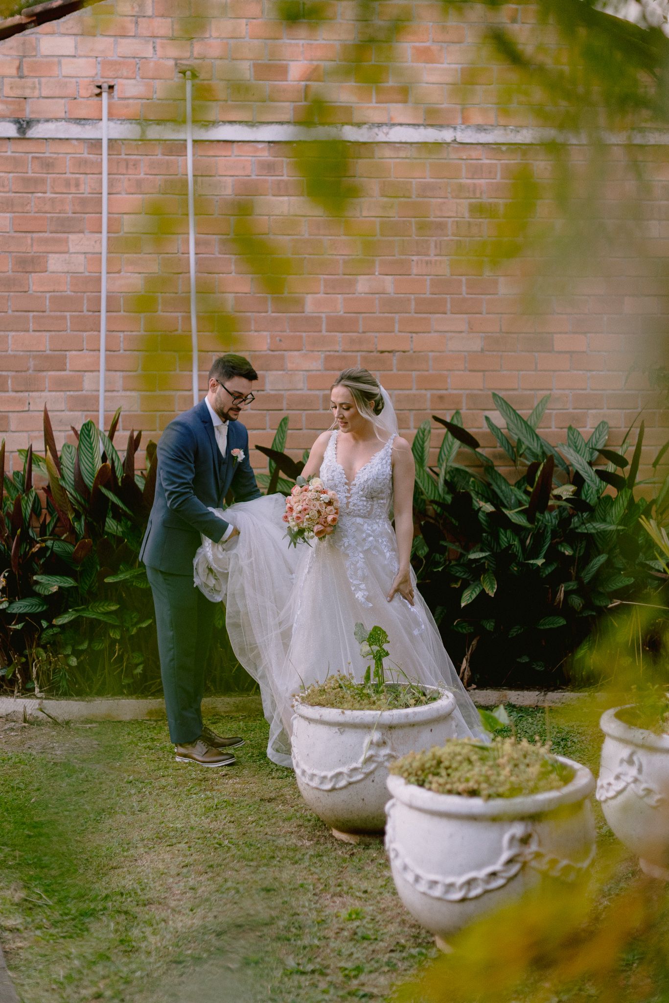 A romantic garden wedding photoshoot featuring a long veil and brick wall backdrop.