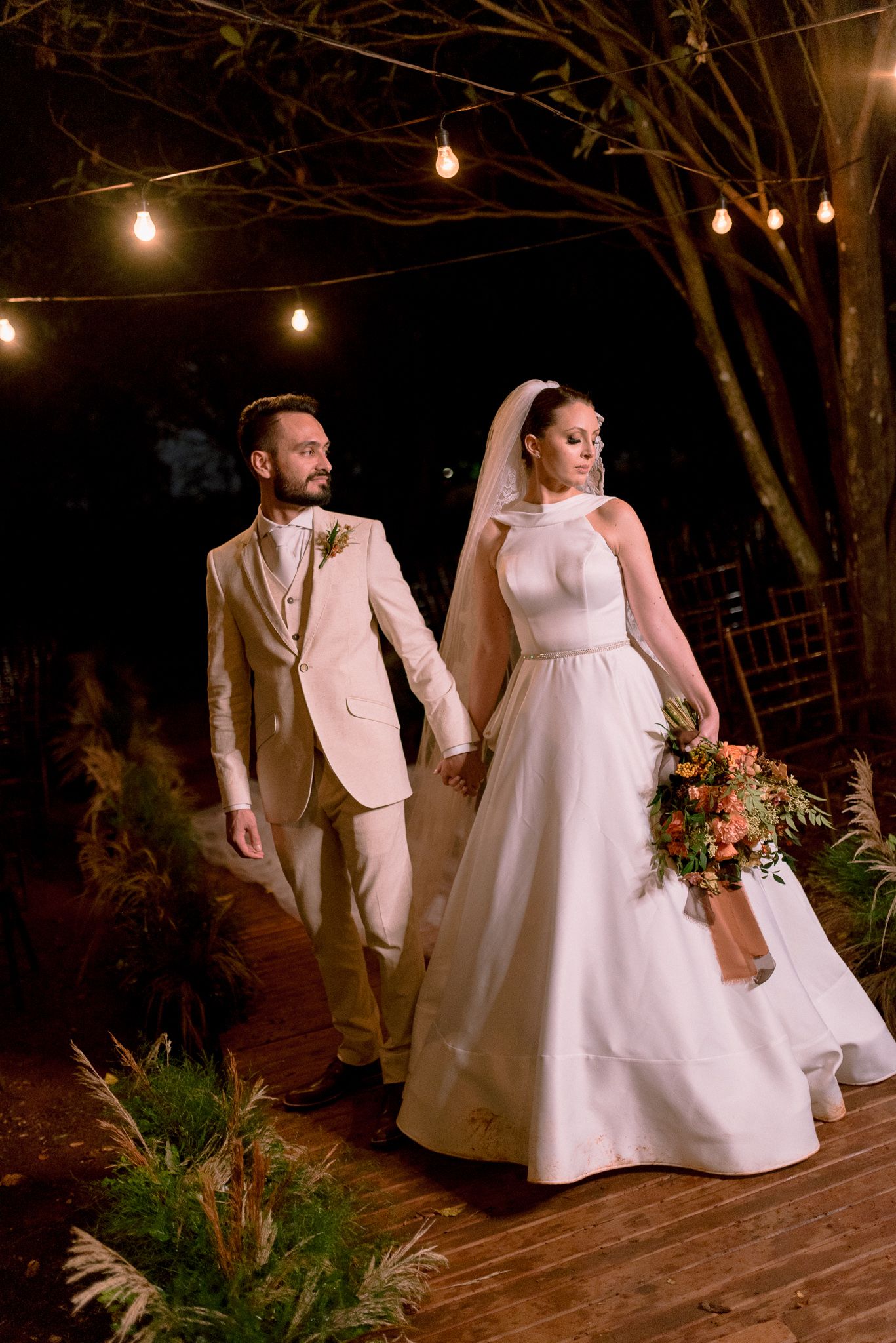 Couple walking together on a wooden deck at night illuminated by string lights.