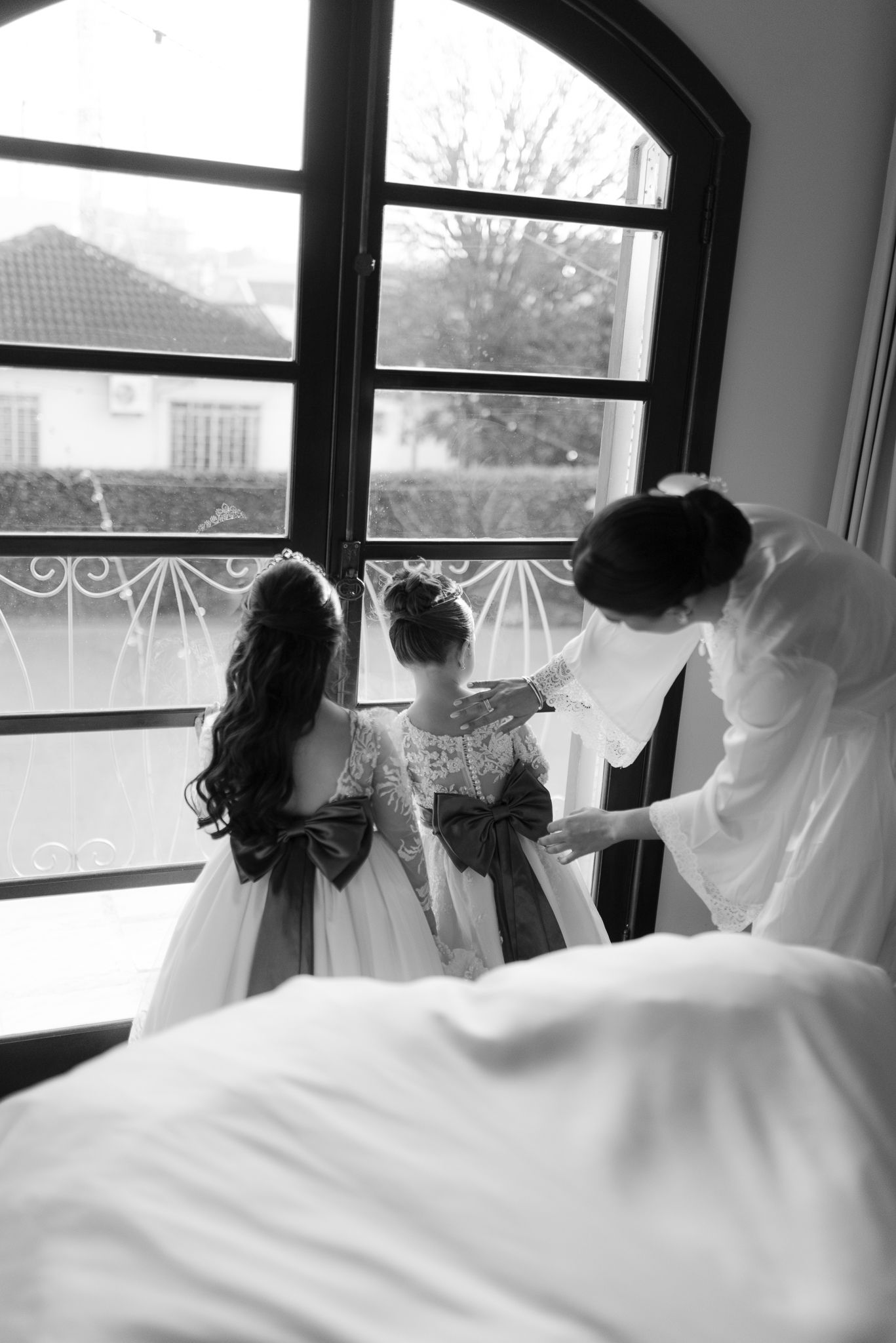 Black and white photo of wedding dresses hanging by arched windows.