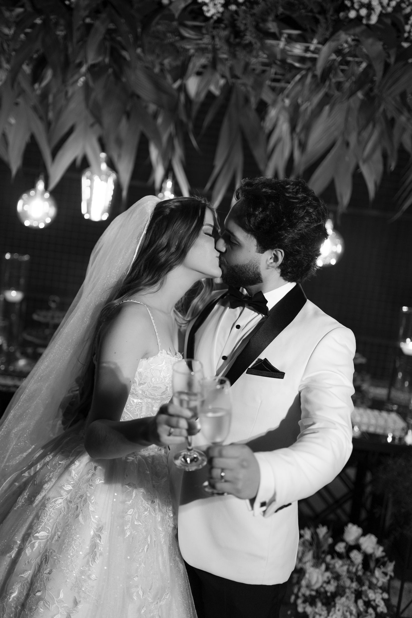 A black and white photo series shows a couple sharing their first kiss as newlyweds during their wedding reception.