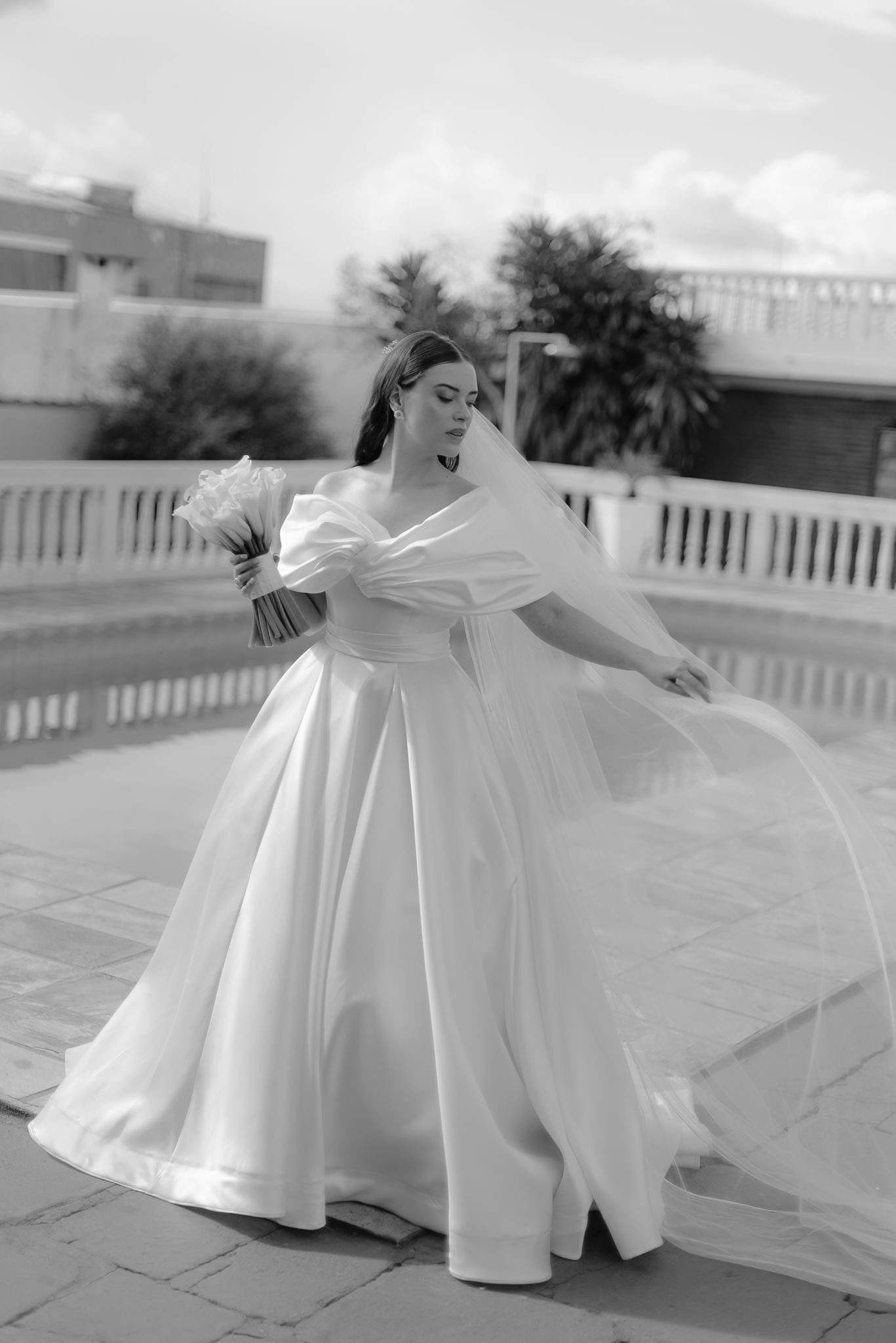 A joyful moment captured in black and white showing someone twirling in an elegant white ballgown on a patio.