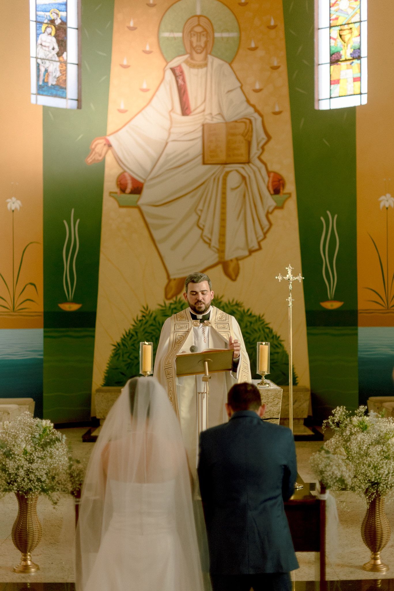 Cinematic panorama of a bride and groom standing at altar during wedding ceremony in church with ornate wall murals.