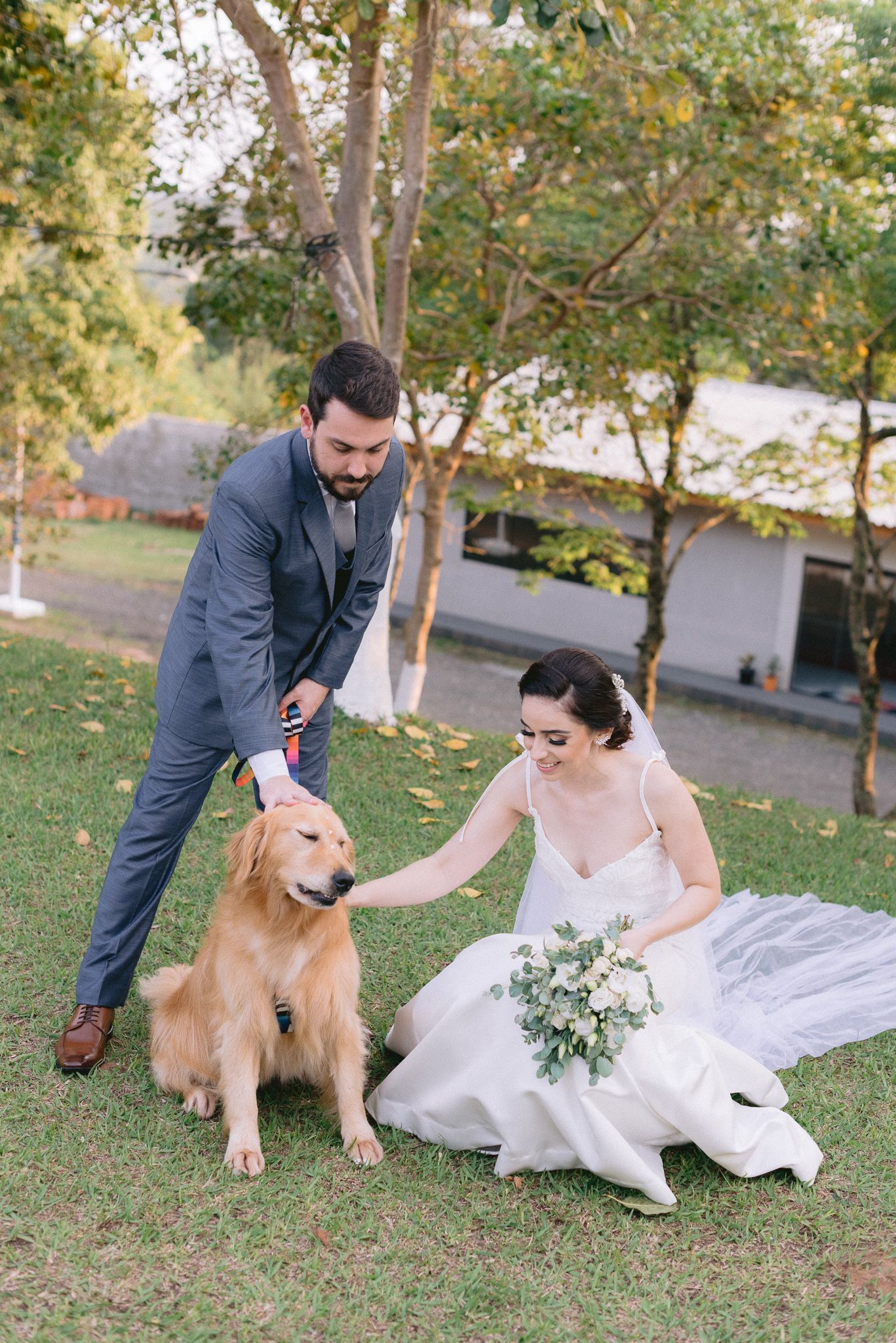 Newlyweds sharing a moment with their golden retriever on grassy lawn.