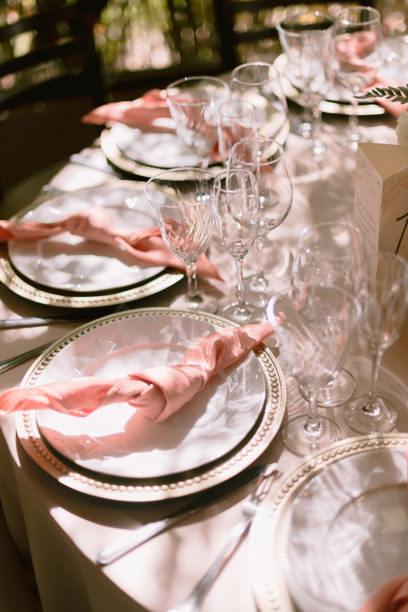 Formal place settings with crystal glassware and coral napkins at wedding reception.