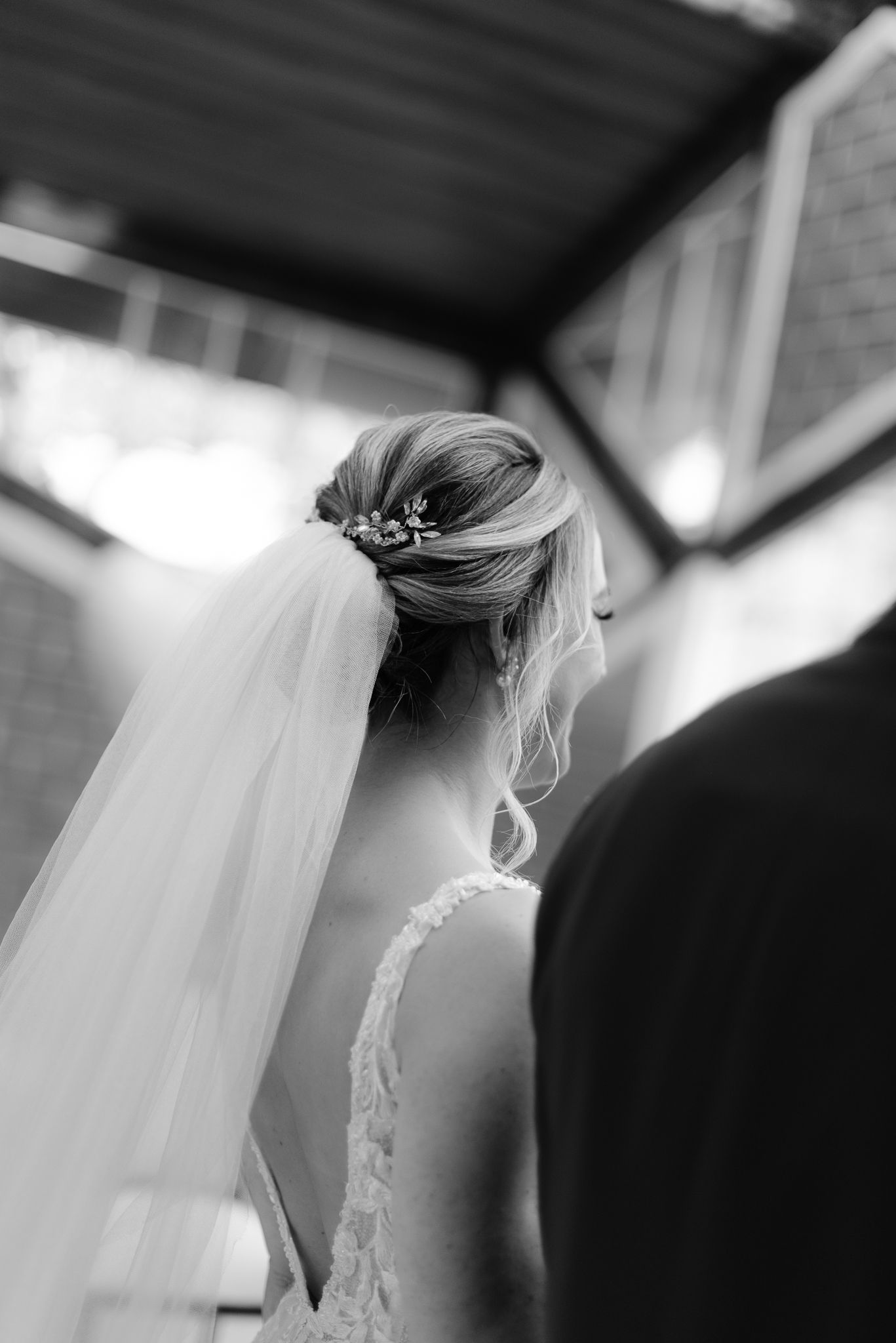Black and white close-up of a bride's elegant updo hairstyle with veil and floral accessories.