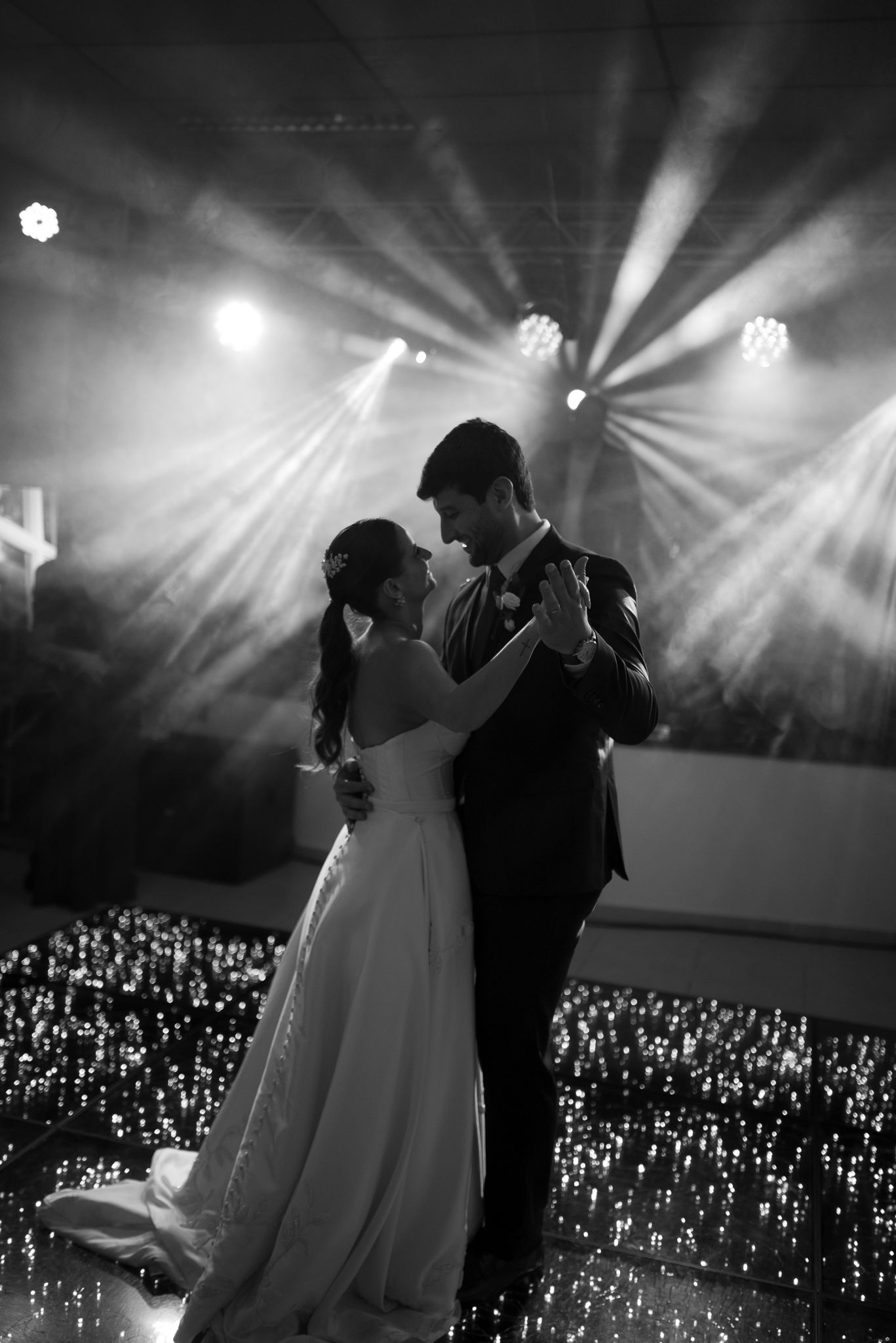 A couple shares their first dance on an illuminated floor surrounded by twinkling lights at a wedding reception.