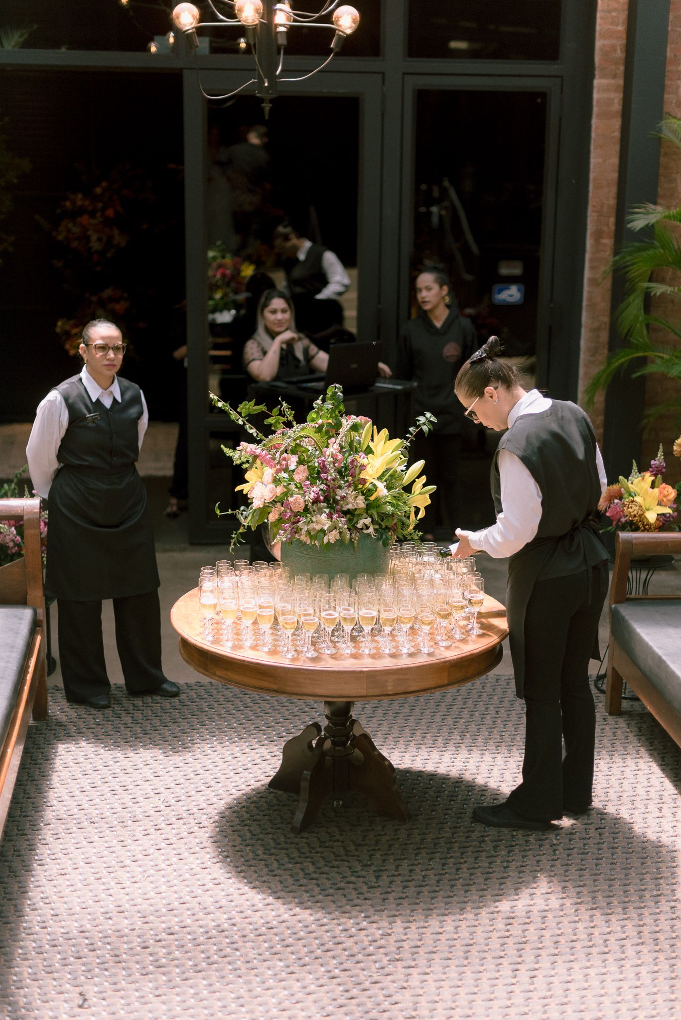 Service staff preparing a round table with champagne glasses and floral arrangements for an event.