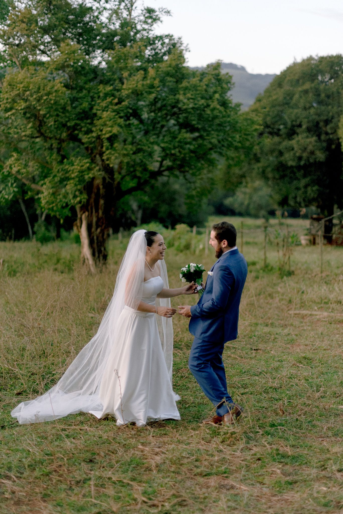 A fresh wedding photo sequence captures a couple playfully dancing together in an open field surrounded by trees.