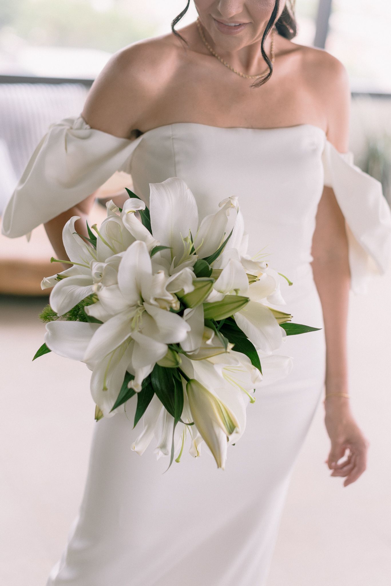 Elegant white wedding dress adorned with cascading white lily bouquet.