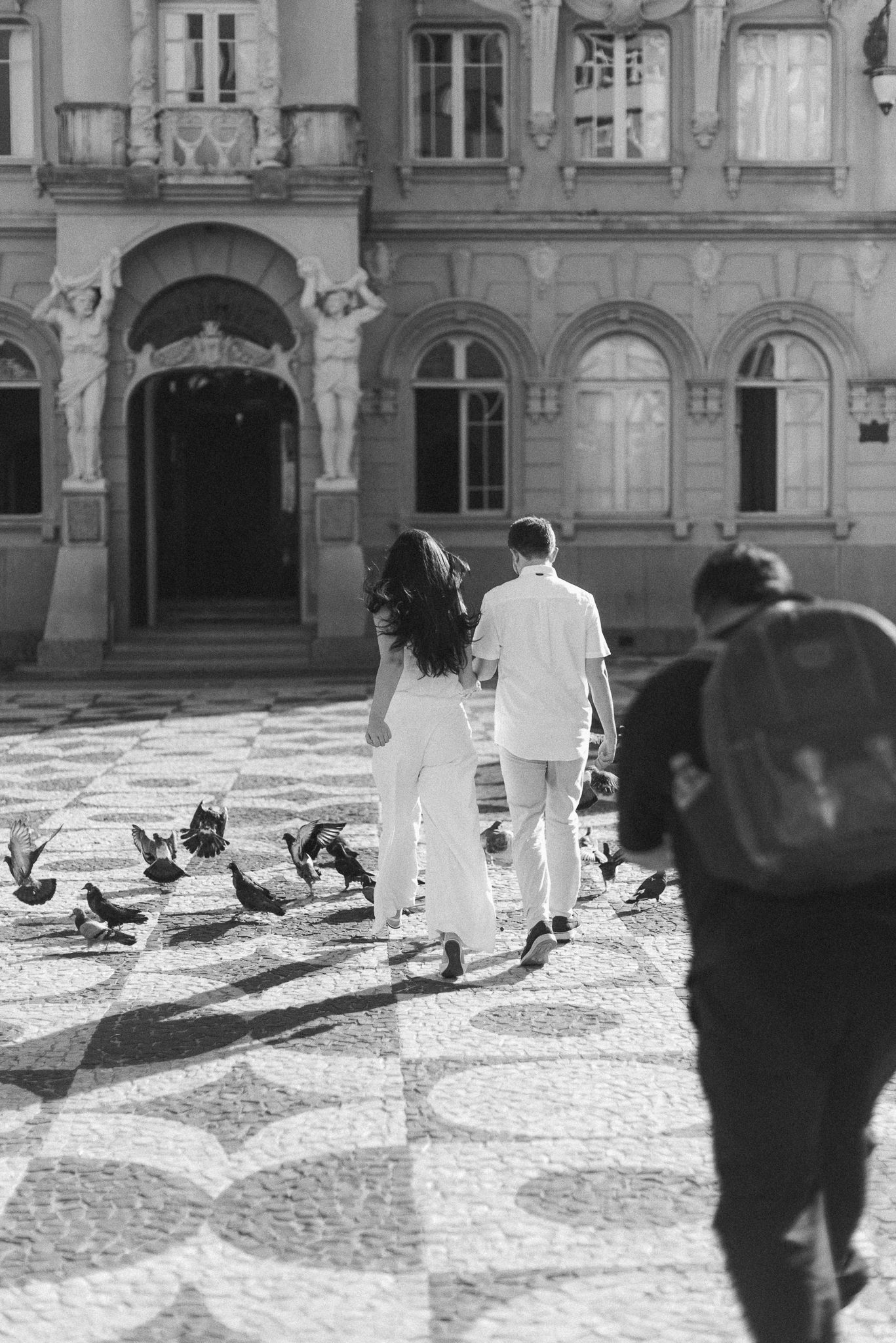 Black and white image of people walking through historic courtyard with pigeons.