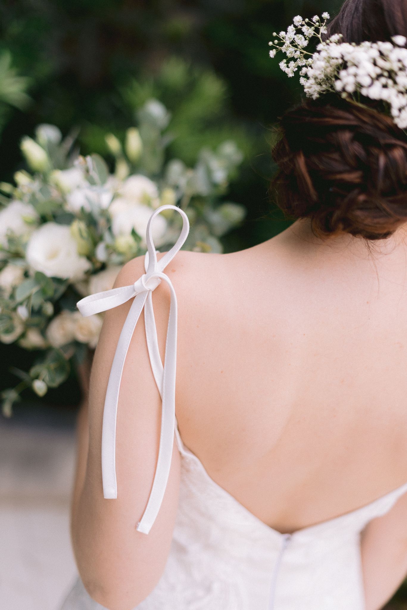 Delicate white ribbon detail on the back of a wedding dress shown against a floral background.