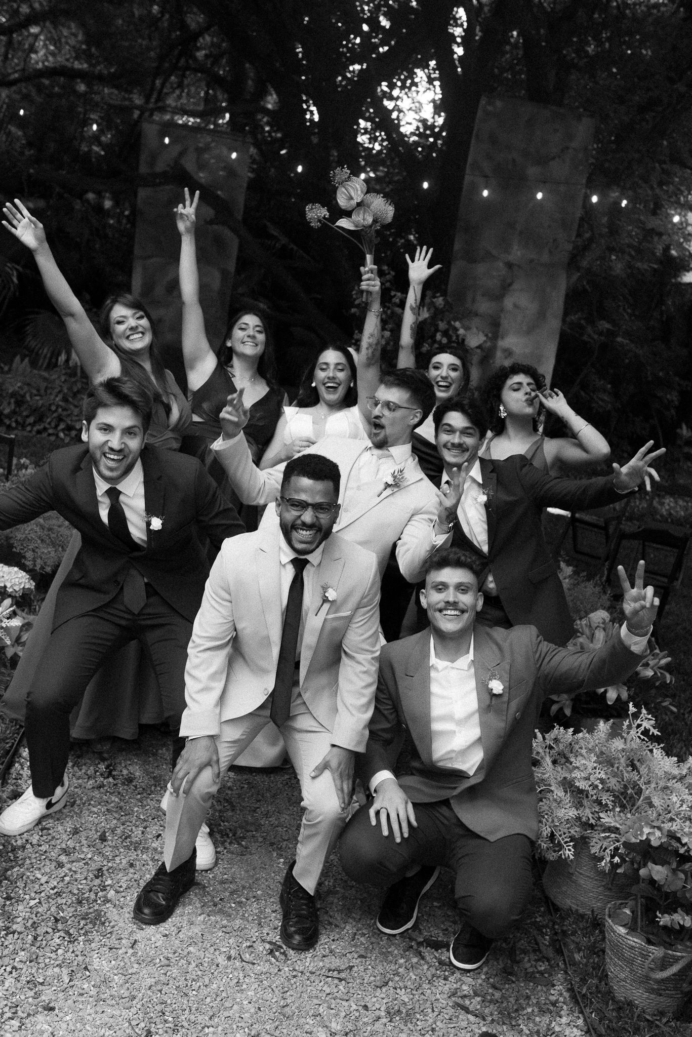 Black and white photo of groomsmen posing playfully on the ground outdoors.