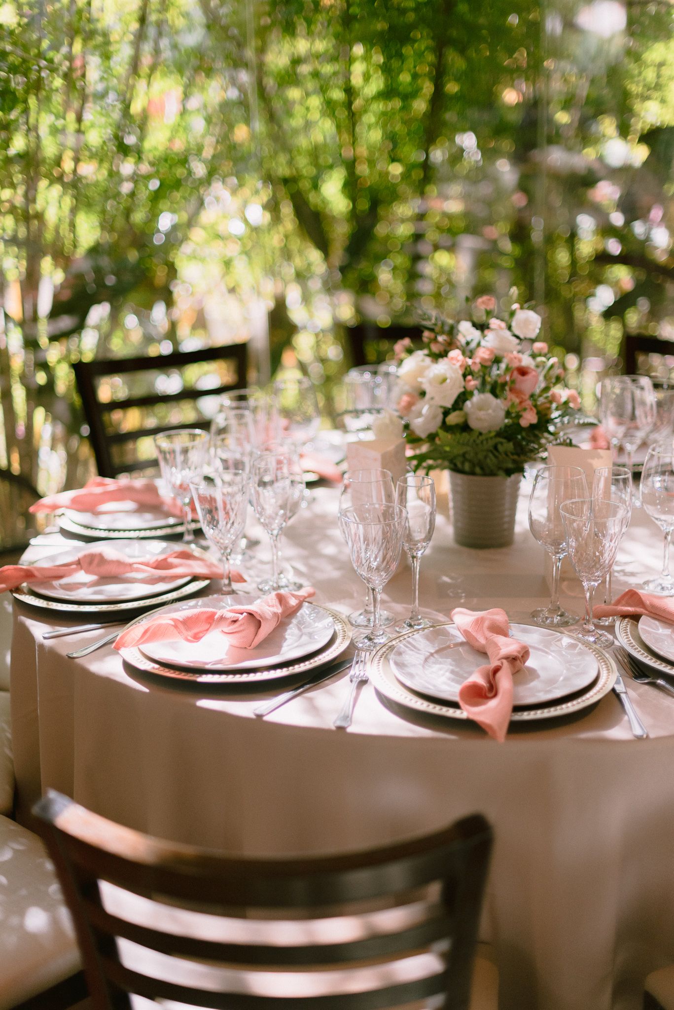 Elegant wedding table settings with pink accents and floral centerpieces in a garden setting.