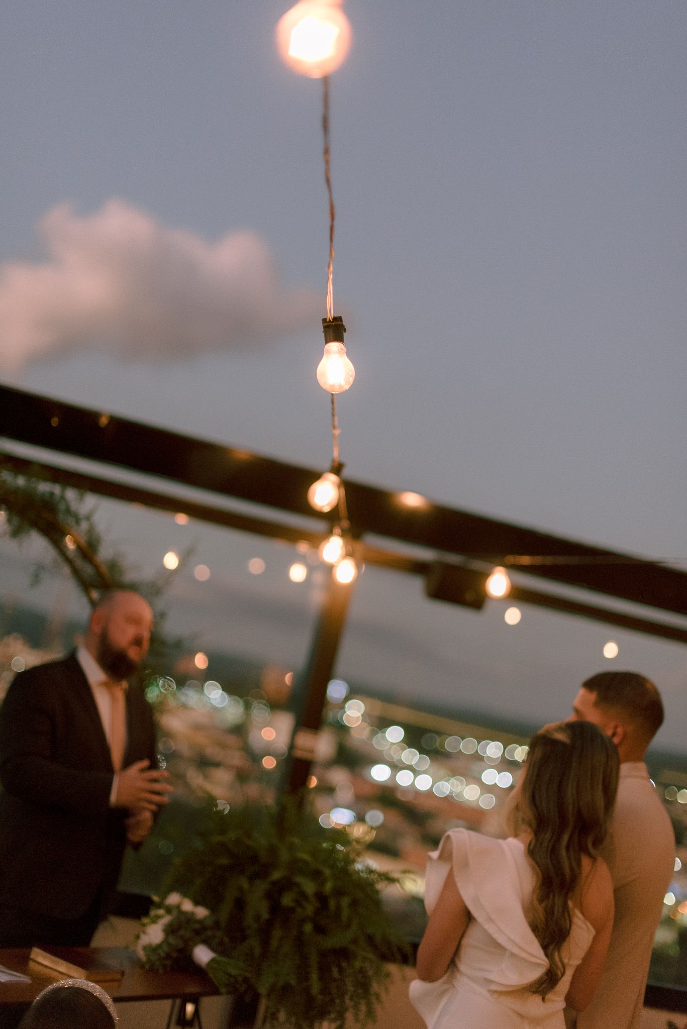 String lights illuminate an outdoor evening gathering with warm ambiance as people mingle beneath the twilight sky.