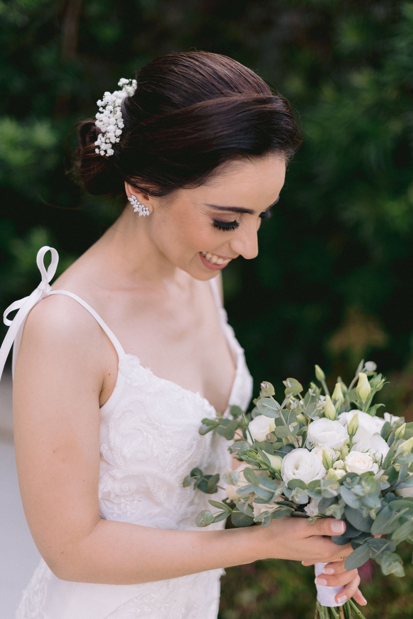 Elegant white wedding bouquet with eucalyptus and roses held against a garden background.