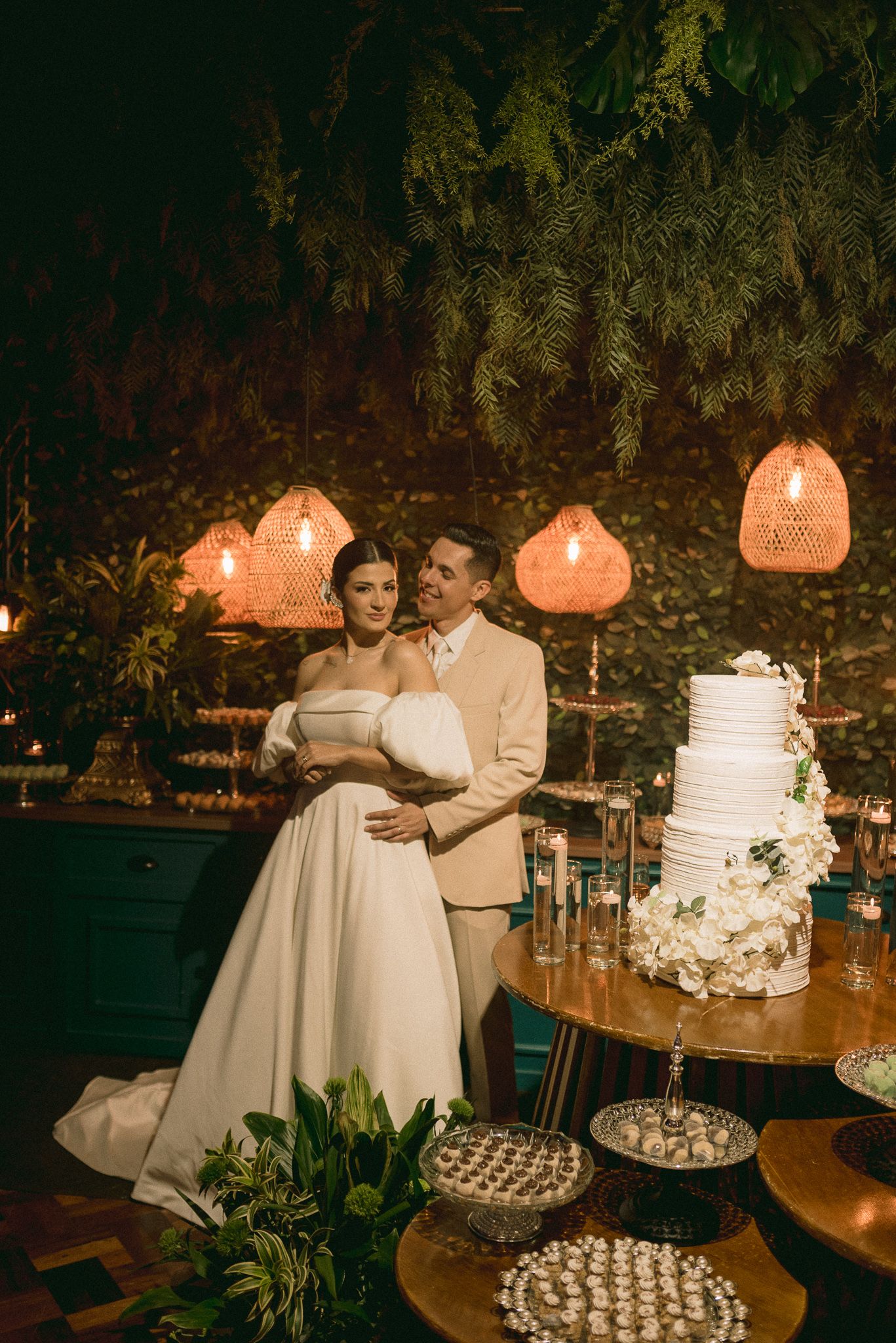 Elegant wedding cake display with warm lighting and coral lanterns creating an intimate dessert table setting.