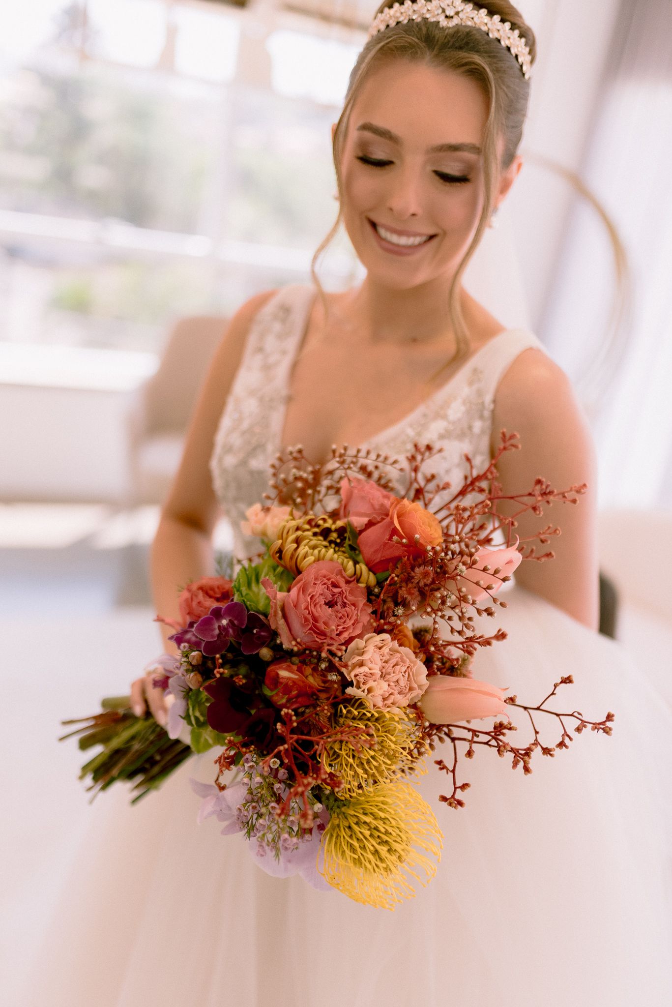 A bridal bouquet featuring vibrant yellow protea, coral flowers, and burgundy blooms in a romantic wedding setting.