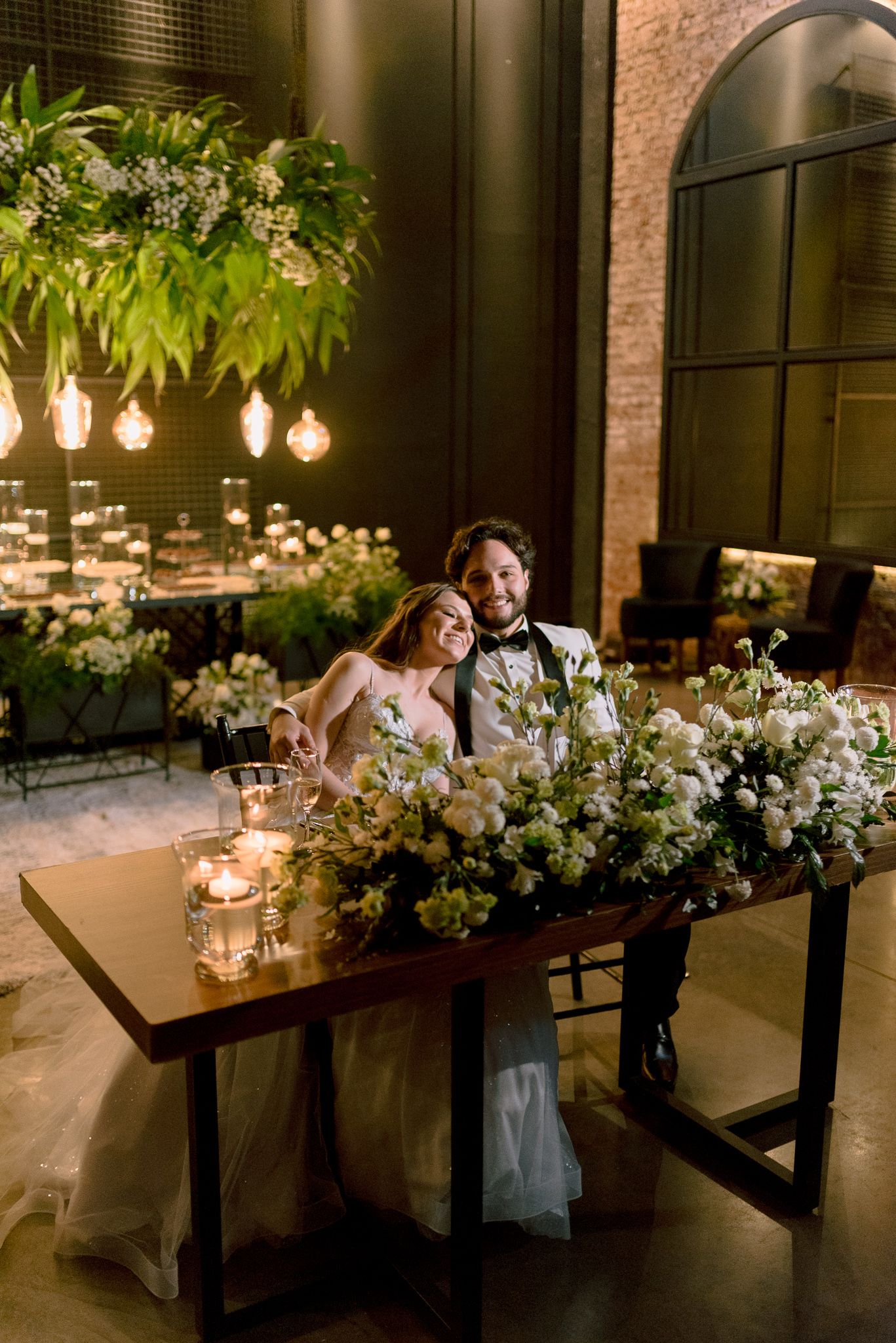 Modern industrial wedding venue decorated with romantic candlelight and lush white floral centerpieces at dusk.