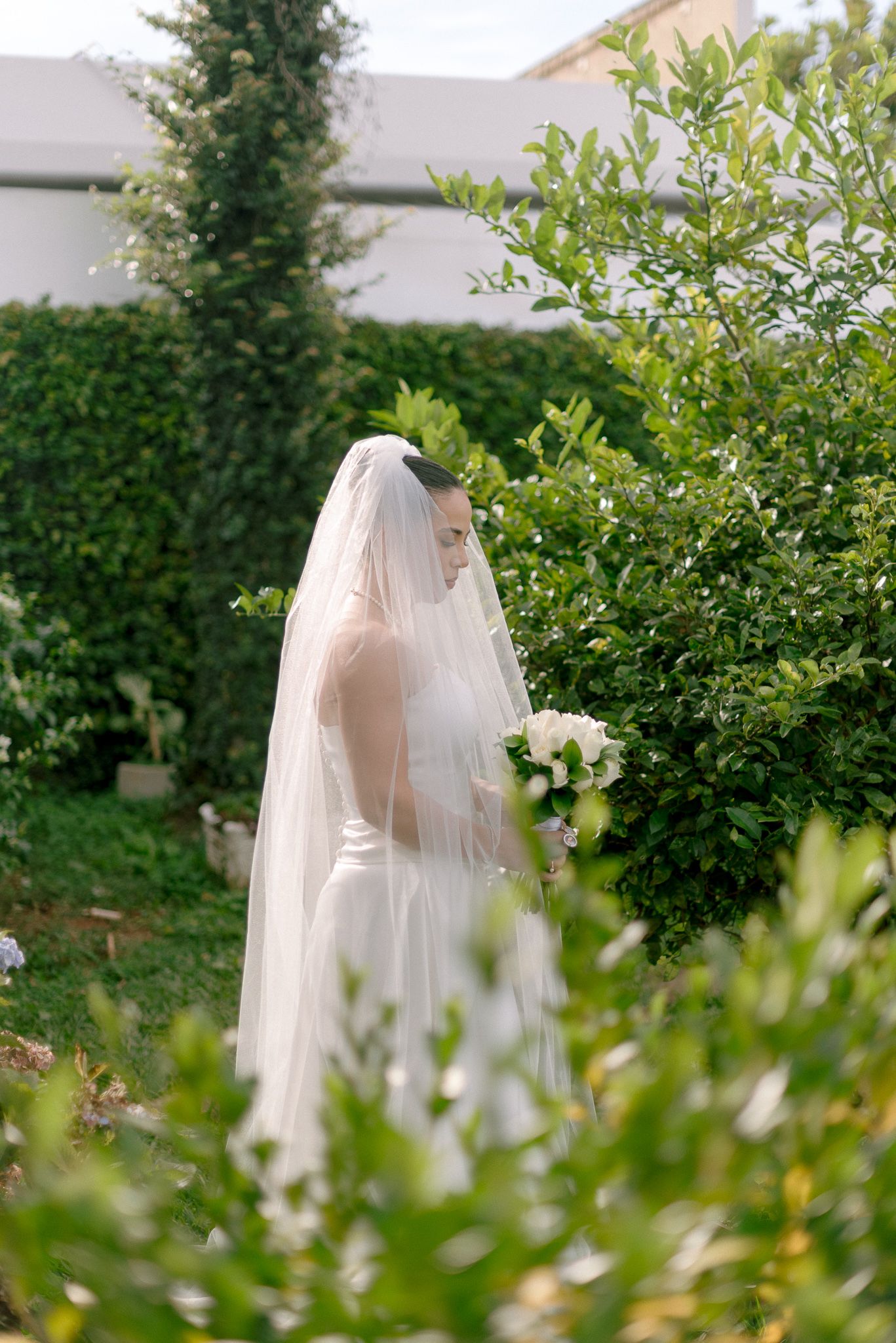 A wedding dress and veil in a lush garden setting with green foliage and natural lighting creates a dreamy atmosphere.