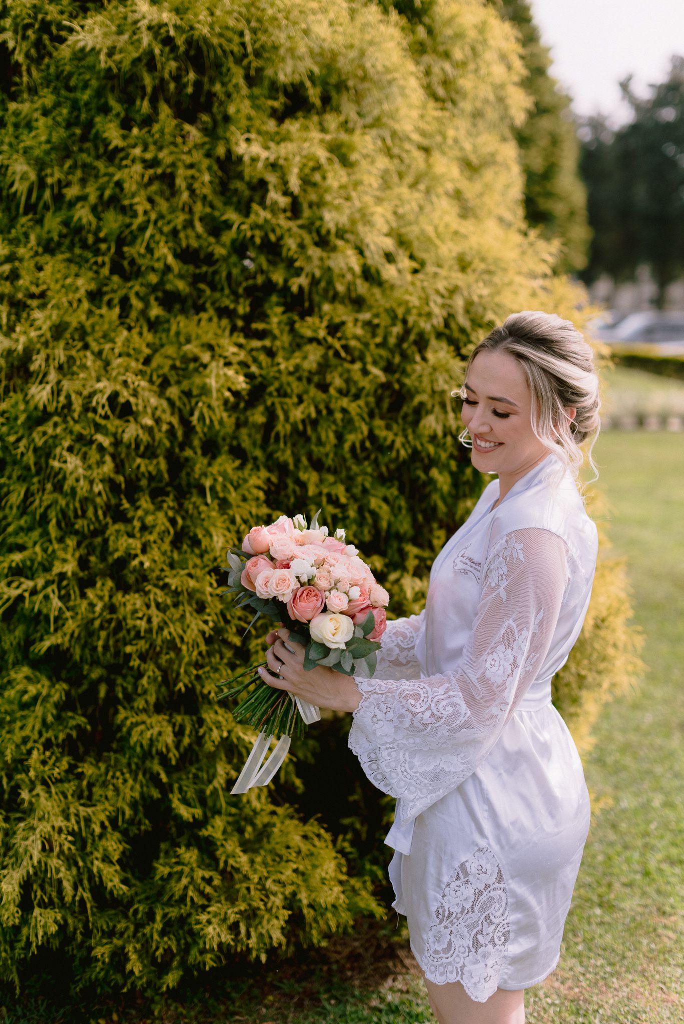 Romantic outdoor bridal portrait with delicate lace dress against evergreen backdrop.