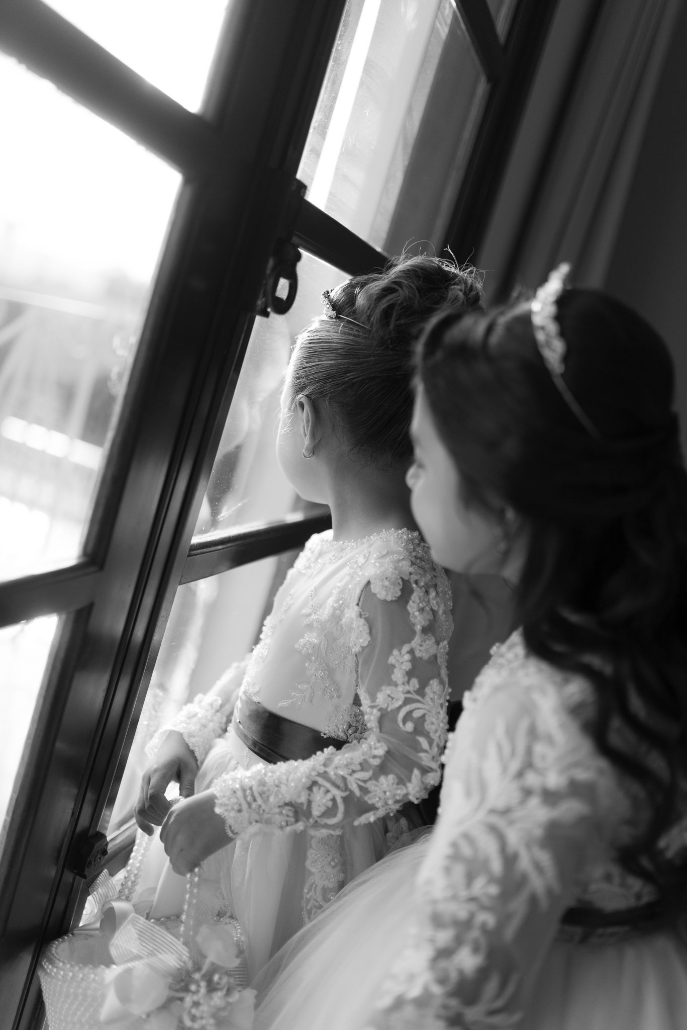 Elegant wedding detail shots show a bride in a lace sleeve gown gazing out a window in black and white.