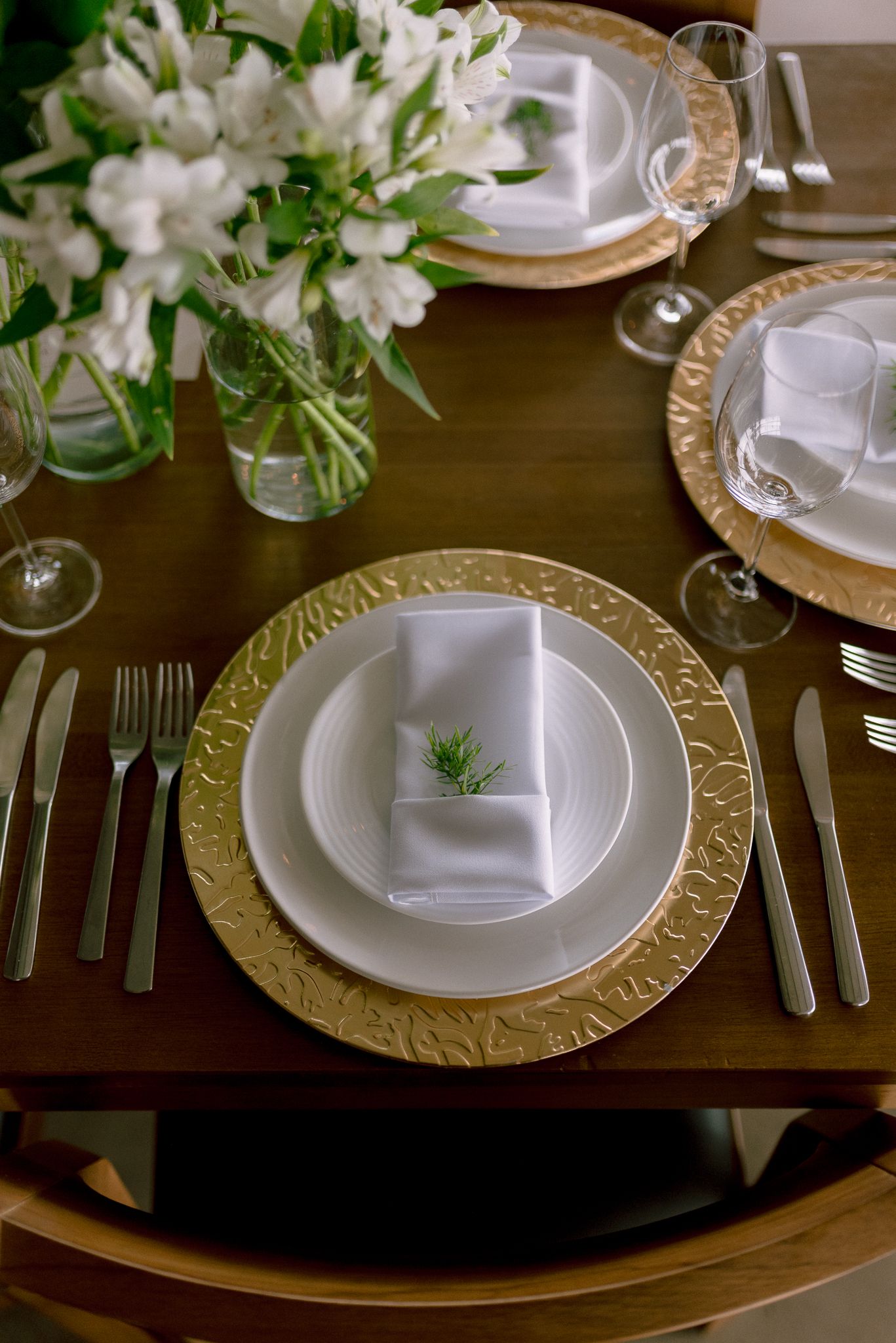 Formal table setting with gold charger plates and white floral centerpieces.