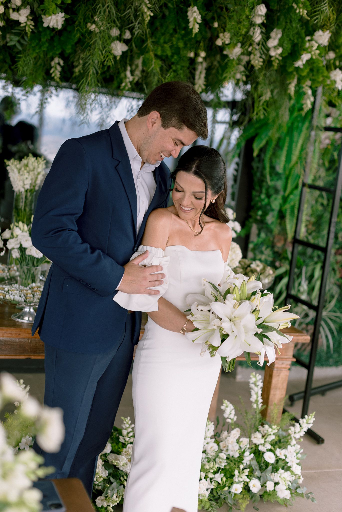 Elegant couple shares intimate moments among white floral arrangements and greenery.