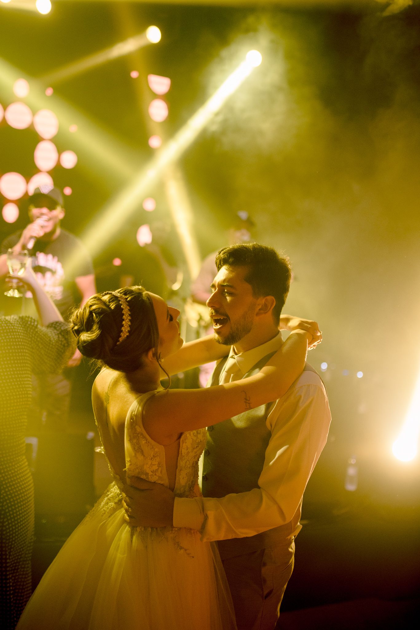 A couple shares their first dance at a wedding reception under dramatic yellow stage lighting and floating bokeh effects.
