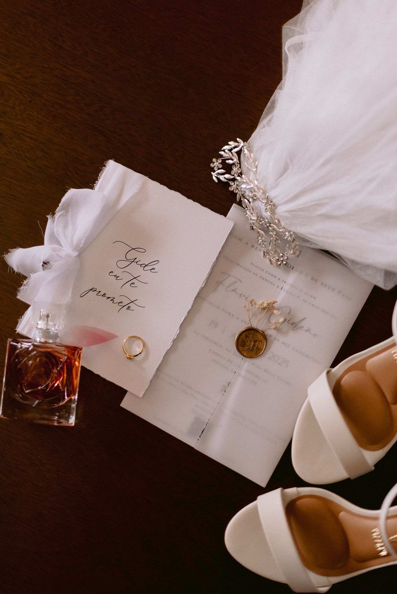 Artistic silk chiffon draping over wedding invitations, rings, and perfume bottles creates an ethereal bridal flat lay.