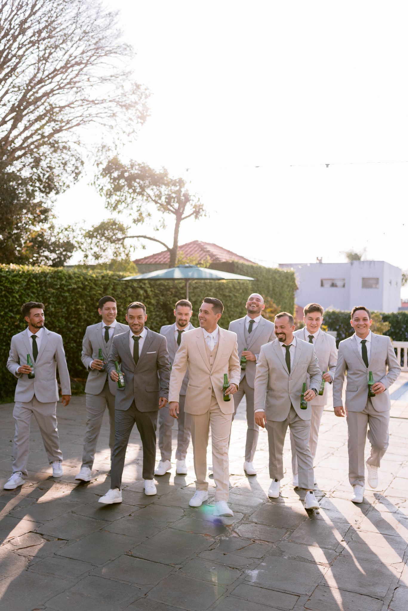 Groomsmen in light colored suits lined up for a formal wedding photo outdoors.