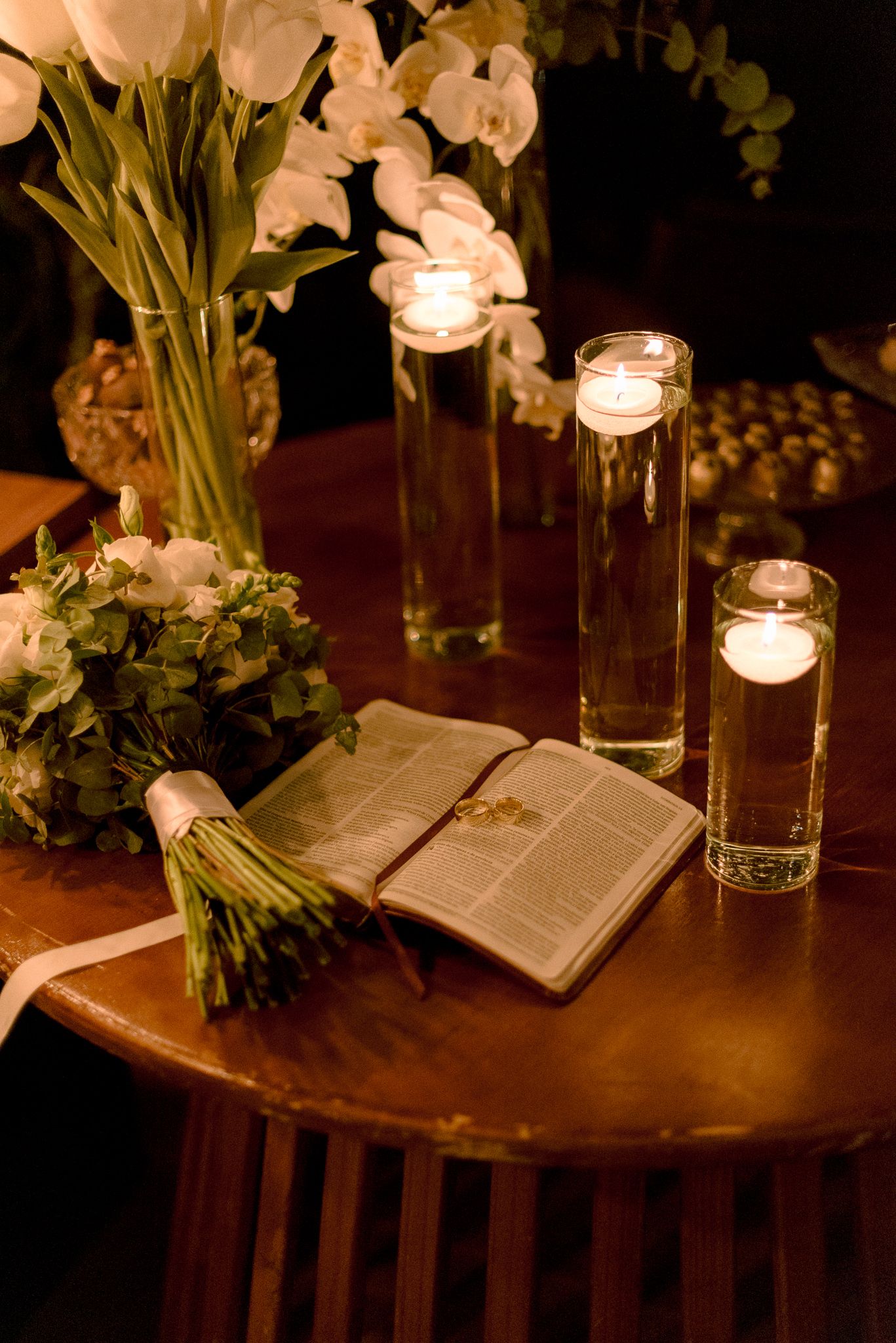 Candlelit table with an open book and white flowers in glass vases creates a romantic evening ambiance.