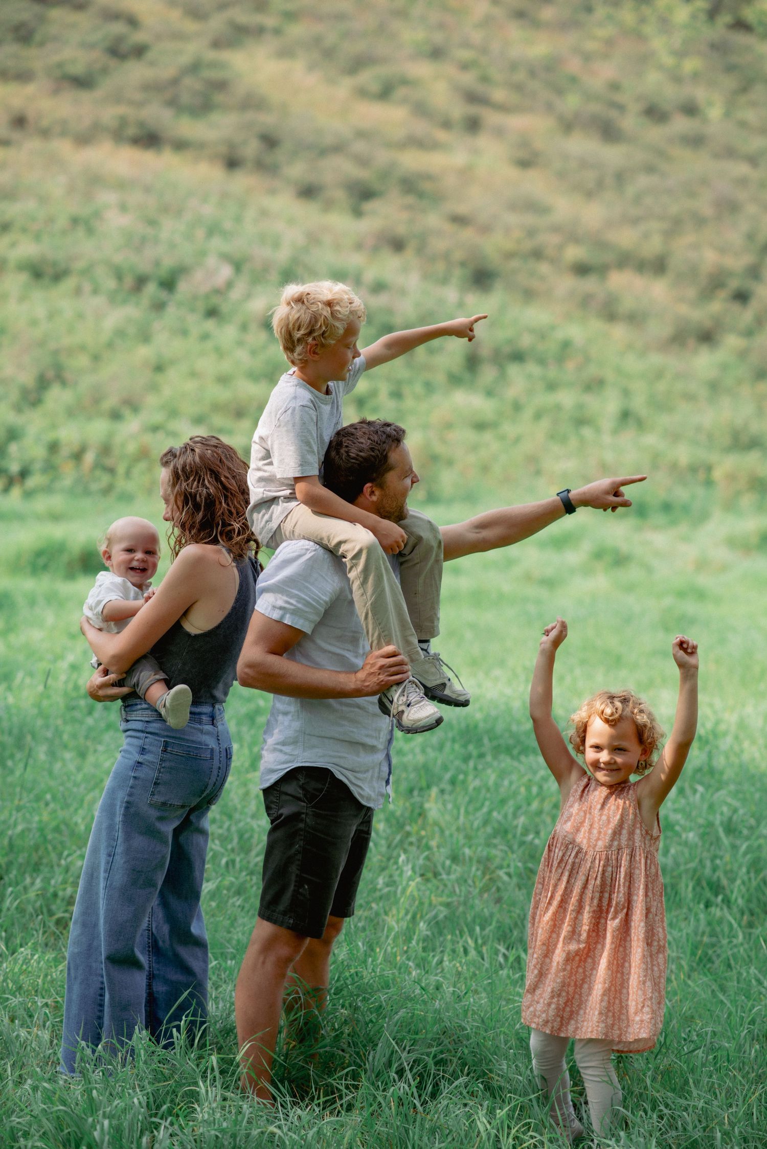 Professional family photos Alberta, dad carrying toddler on shoulders, daughter dancing, mom holding baby during outdoor session