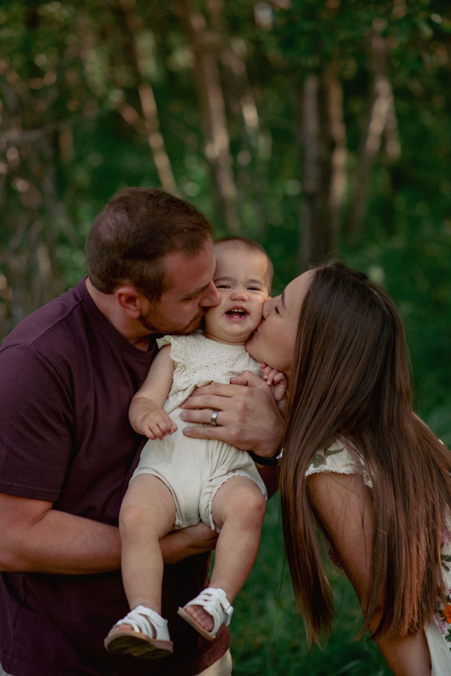 Family photography in Nose Hill Park Calgary, parents kissing one-year-old daughter during outdoor session