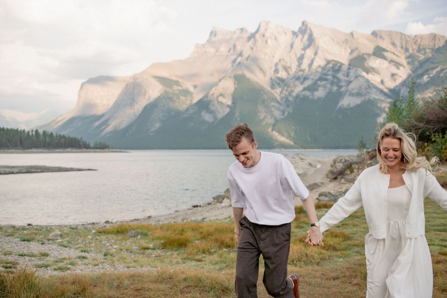 Lake Minnewanka engagement photography Alberta, romantic moment of couple running hand-in-hand outdoors