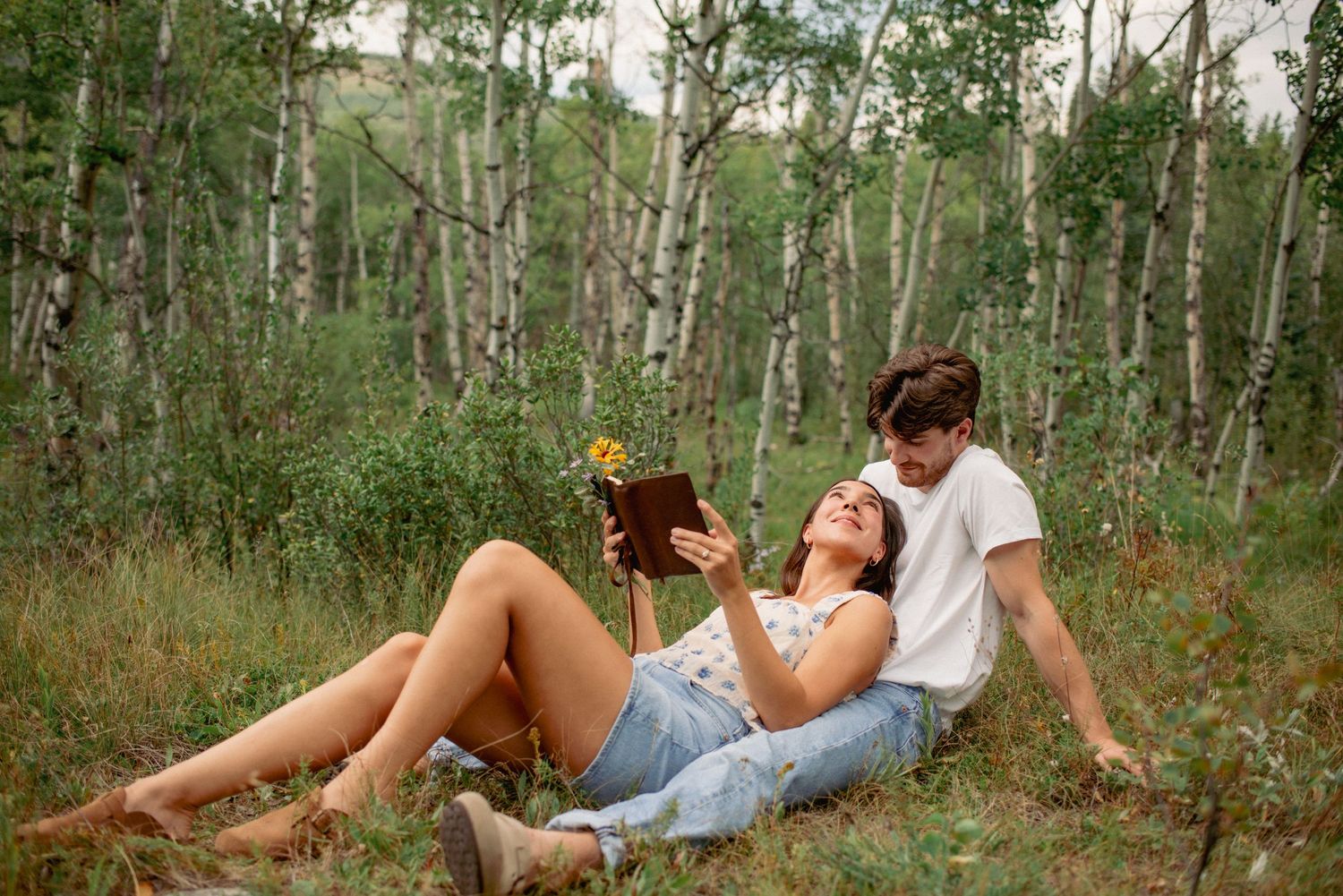 Outdoor couple session Alberta, romantic moment with partner reading in fiancé’s lap