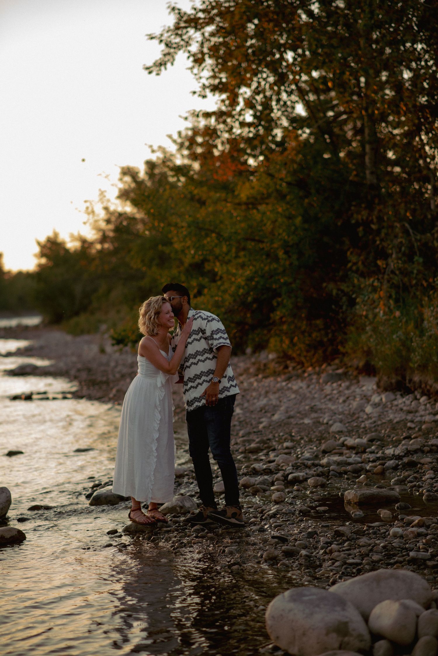 Couple photography near Cochrane Alberta, partners whispering a secret by riverside