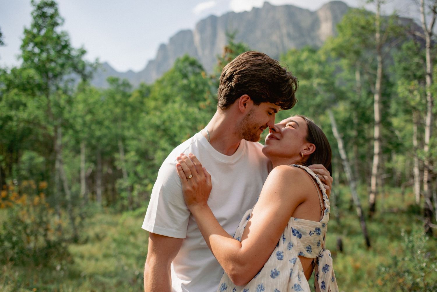 Outdoor couple photography Rocky Mountains Alberta, partners leaning in for kiss with scenic mountain