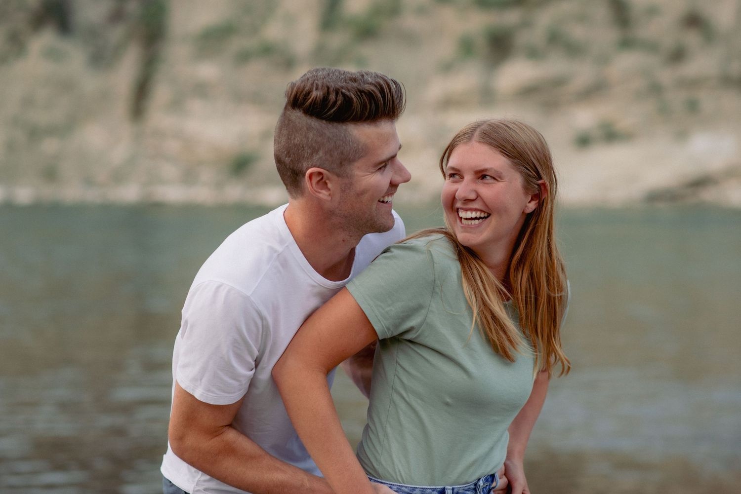 Outdoor couple photography Cochrane, partners sharing joyful tickling moment by river
