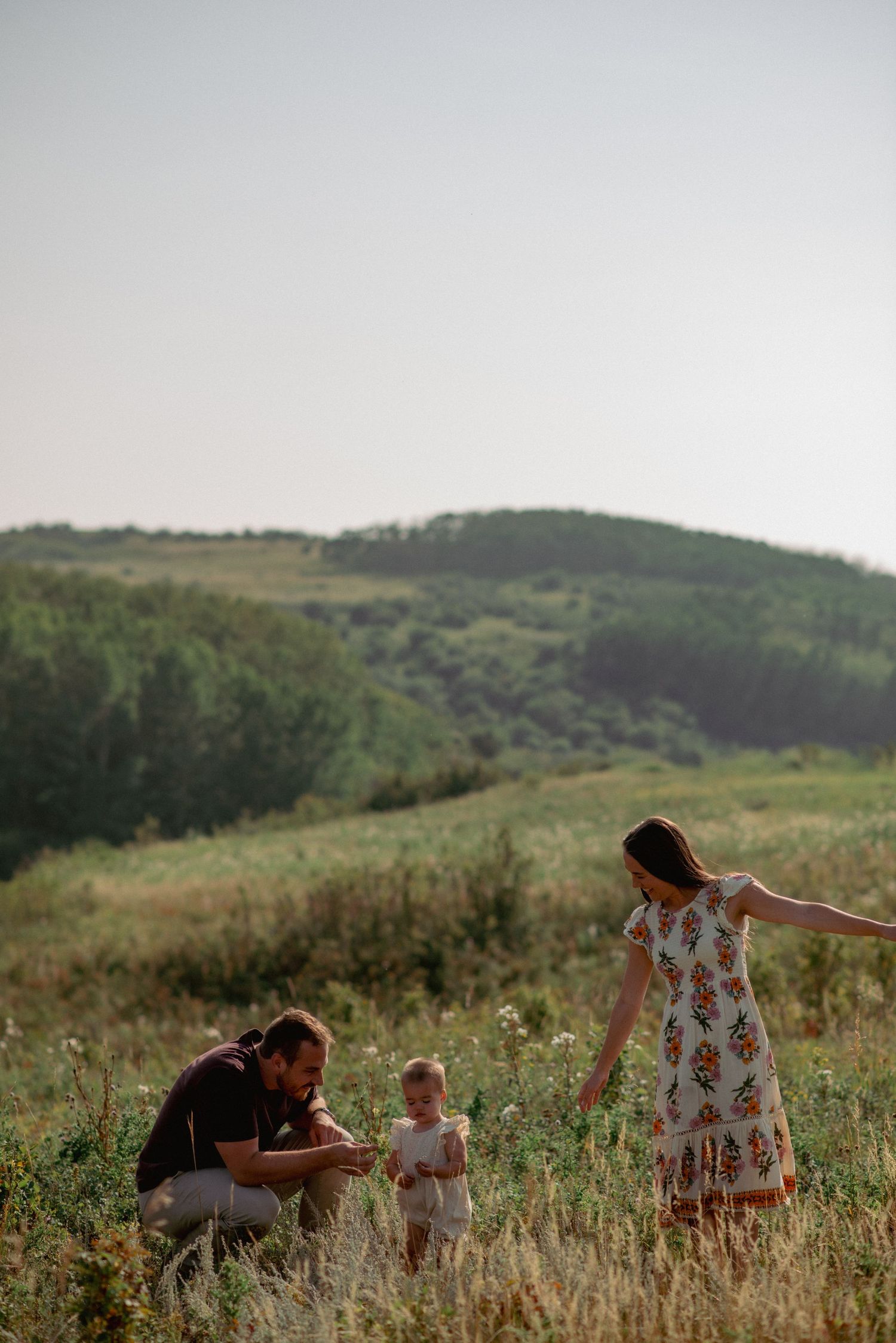 Professional family photographer Calgary, parents and one-year-old daughter playing in Nose Hill Park