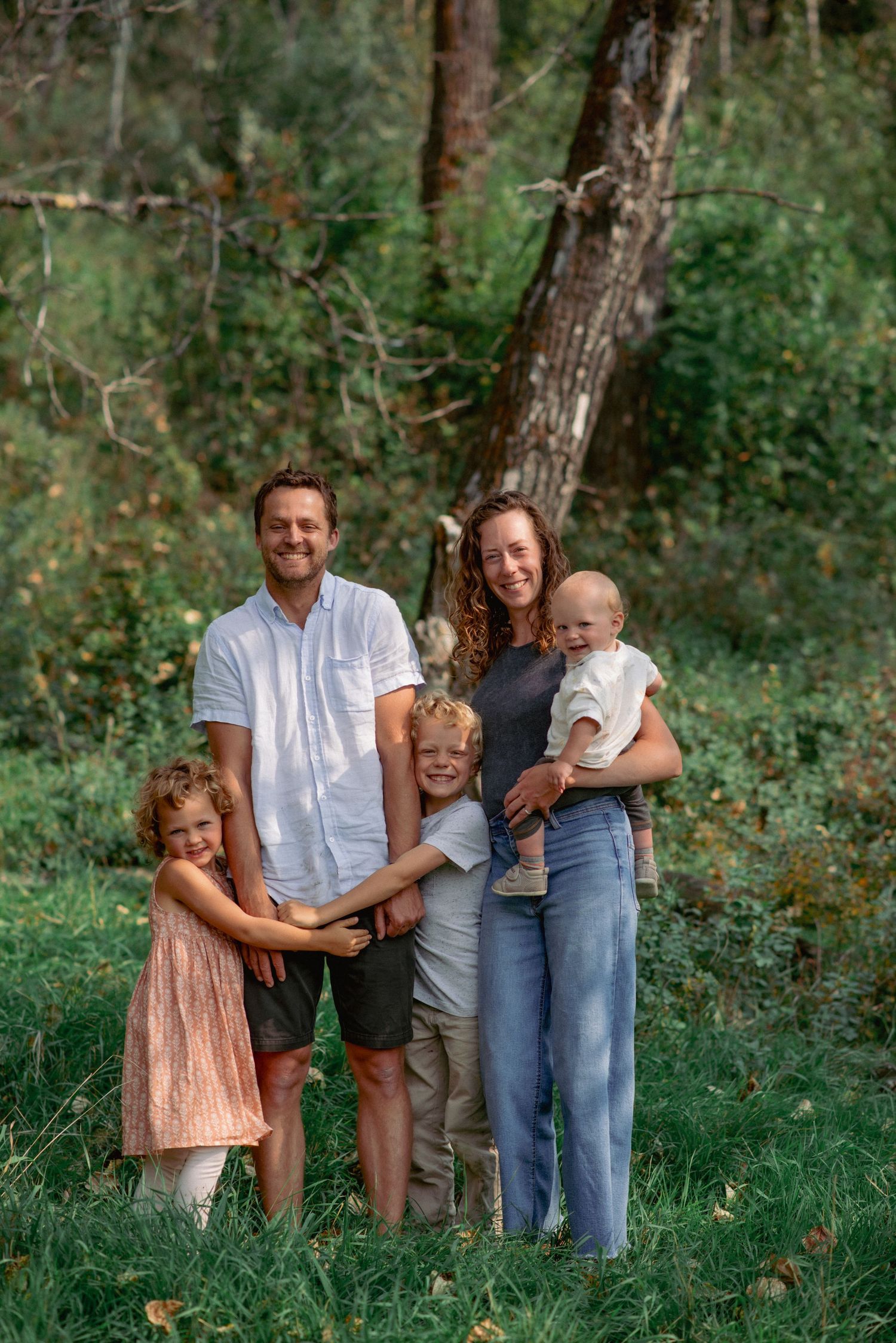 Professional family photos Alberta, parents and children smiling at camera in scenic forest