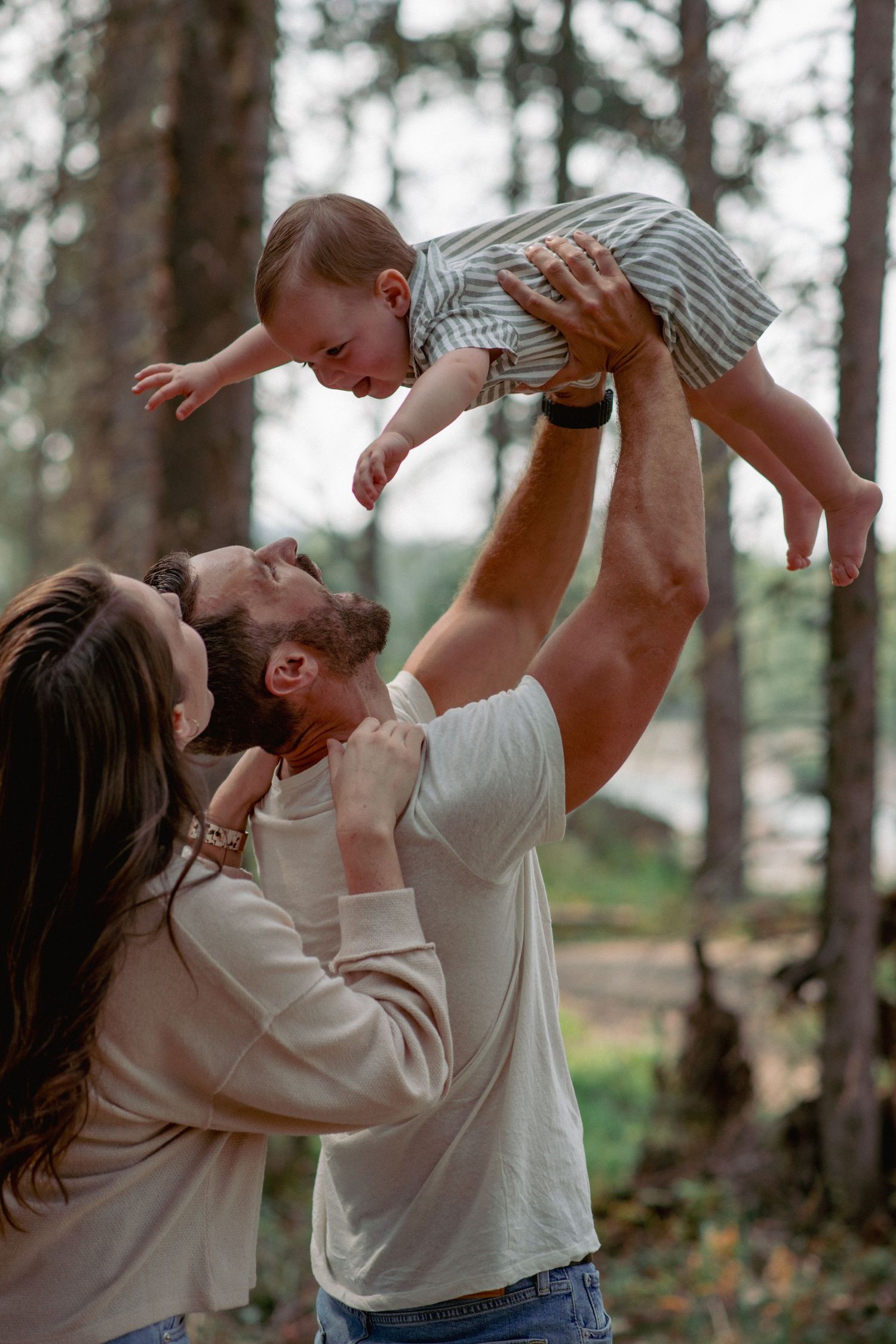 Candid family photography Bragg Creek, toddler thrown in air by dad while parents share loving gaze