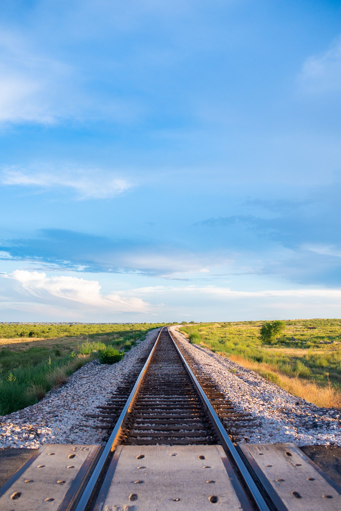 Railroad tracks extending into horizon under bright blue sky with gravel ballast.