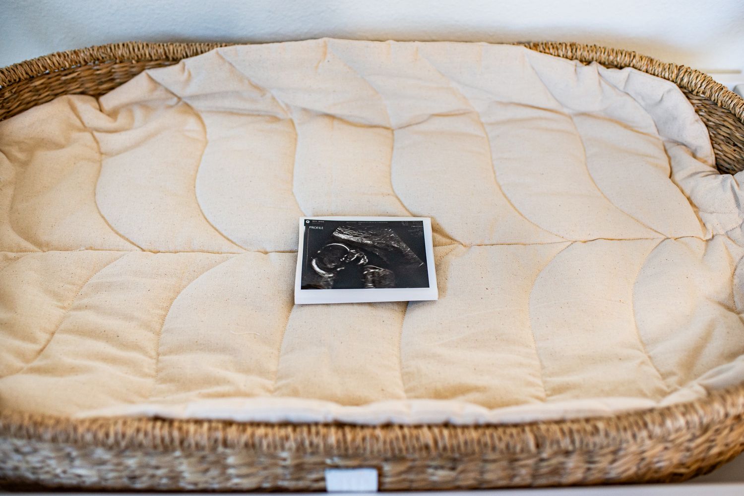 Close up view of a white quilted mattress pad in a woven basket.
