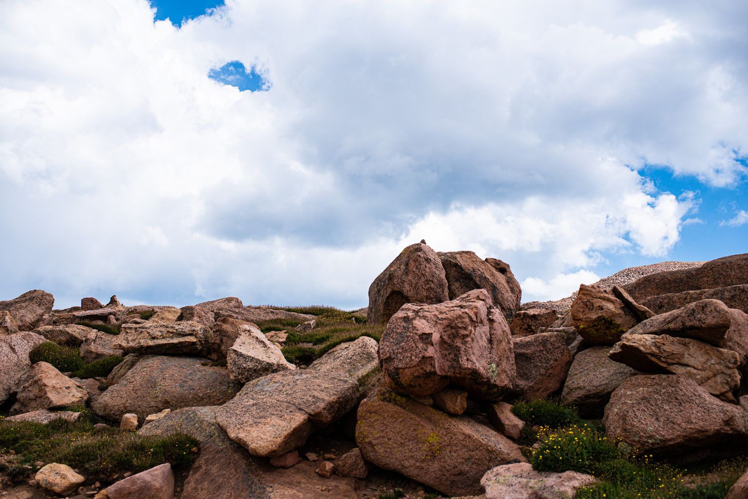 Rocky mountain landscape with large red boulders against cloudy blue sky.