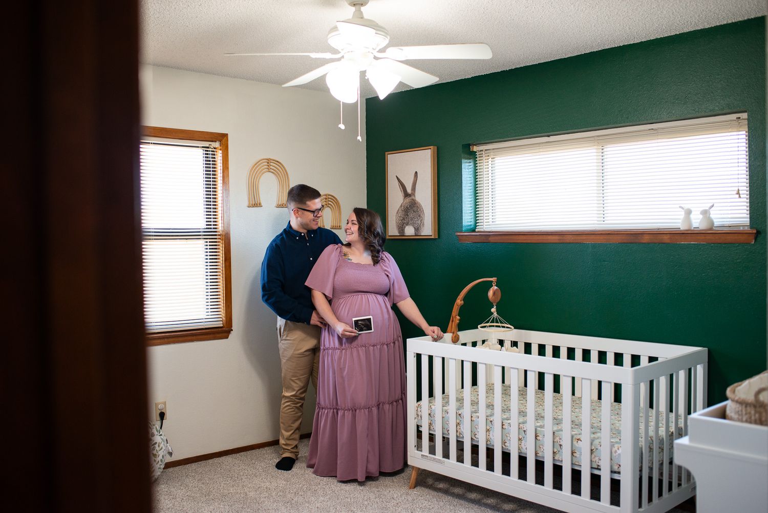 Interior of a nursery with green walls, white crib, and natural lighting.