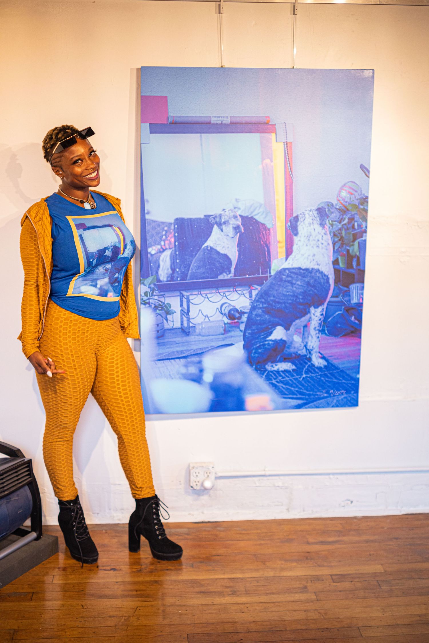 Woman in yellow outfit poses beside large blue art photograph in gallery.