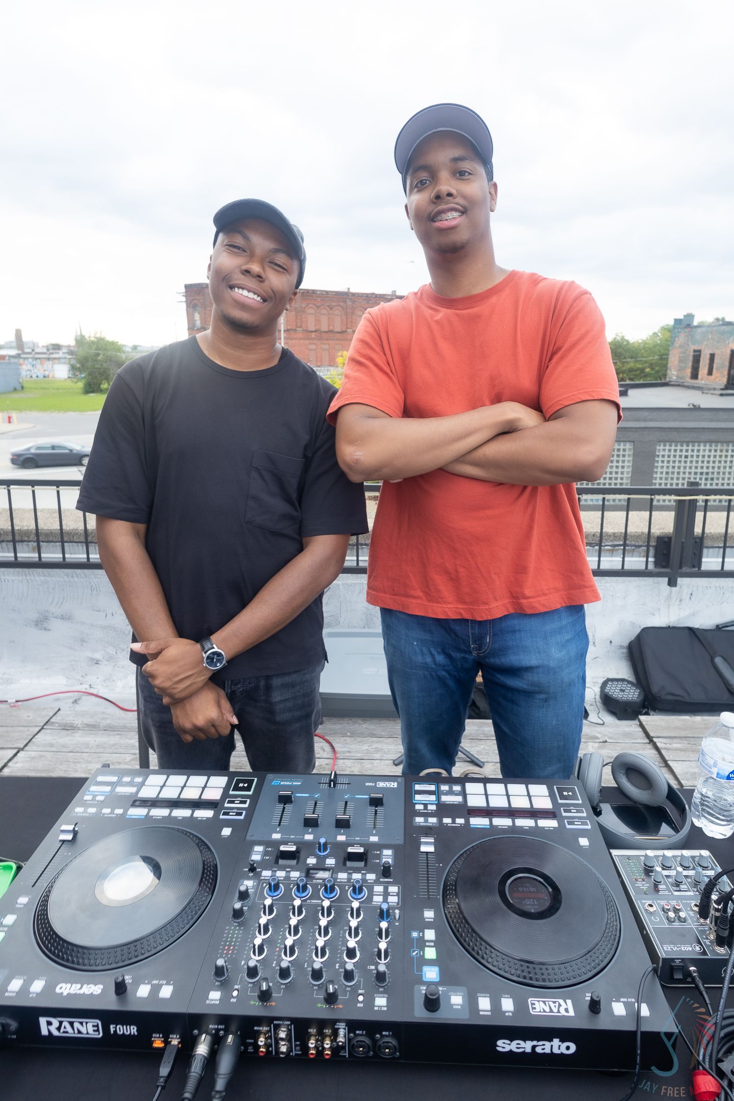 Two young men smiling behind a Rane Four Serato DJ controller on an outdoor rooftop.