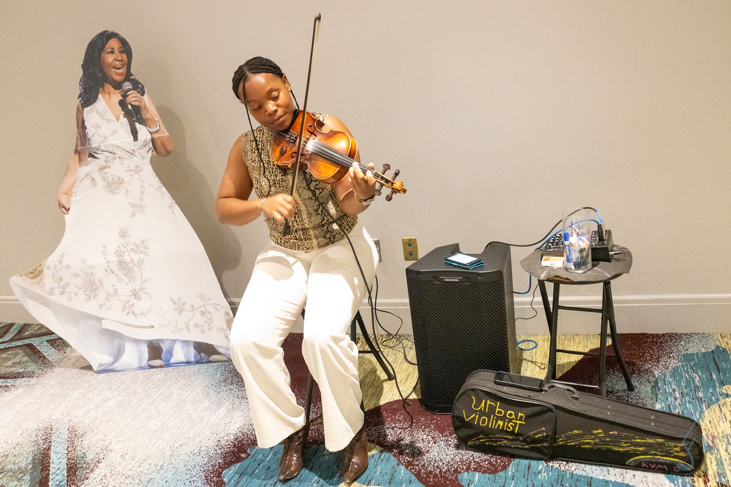 A violinist performs in white outfit beside a life-size cutout of a woman in a wedding dress at an indoor event.