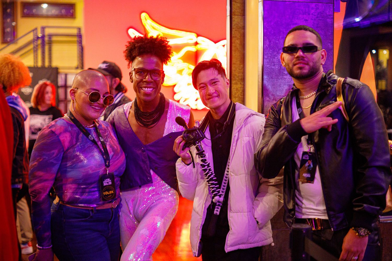 Four stylish friends pose together at a vibrant neon-lit event venue.